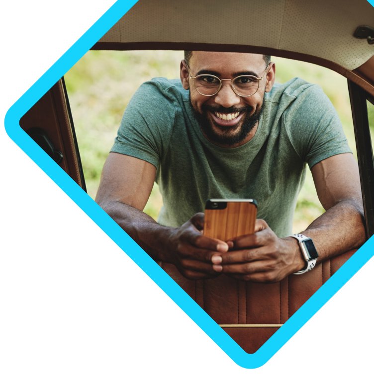 Homem sorrindo apoiado na janela da porta do carro pelo lado de fora com um celular na mão